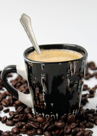 Black cup with coffee surrounded by coffee beansの写真素材