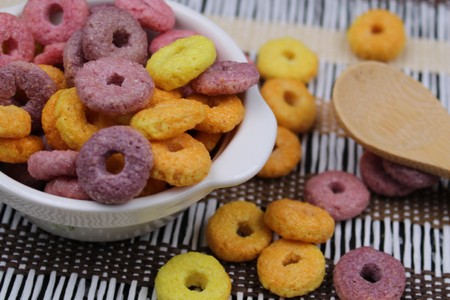 Small white bowl with colorful round cereals and wooden spoon