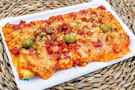 Slice of pizza with ham cheese and green olives on a wicker trivetの写真素材