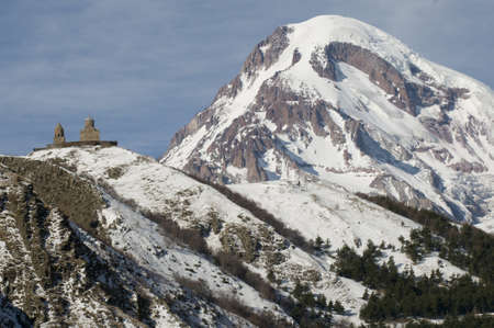 These are Greater Caucasus mountains in winter. Gergeti Trinity Church is situated 	at the bottom of Mount Kazbek.の写真素材
