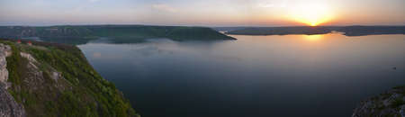 This is a sunset on the lake  The lake is locked in hills covered with spring foliage の写真素材
