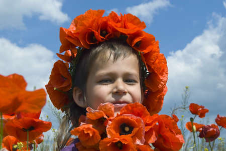 Girl has chaplet of poppies on her head  Poppies also are in the foreground, blue sky with clouds is in the background の写真素材