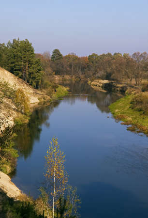 Evening sunlight falls on blue river an highly coloured trees  Gold birch is in the foreground の写真素材
