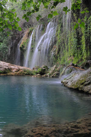 The Kurshunlu Waterfall is located 19 km from Antalya, Turkey  The waterfall is situated in the forest, beautiful lake and branches of fig-tree are in the foreground の写真素材