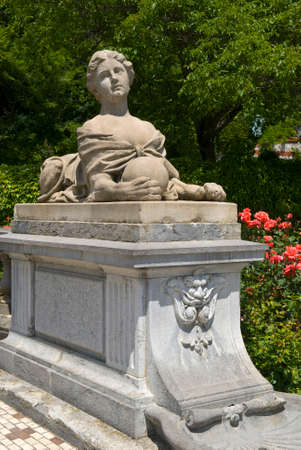 Chimera sculpture against the foliage and red roses. Chimera is an architectural detail of Masandra Palace complex (Crimea).の写真素材
