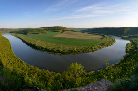 Top view of Dnestr (Dniester) river in springtime. The river surrounds multicolored field. Mountains...