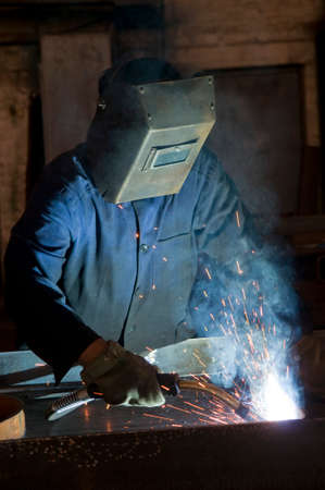 Working man with helmet shield on his head is welding steel construction. Heavy work in the...