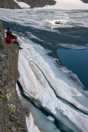 Woman sits on the cliff and  	contemplates mountain lake with float ice. Summer beginning at Deniz...
