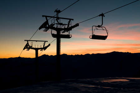 Ski-lift silhouette against beautiful sundown background. Winter season in high mountains.の写真素材