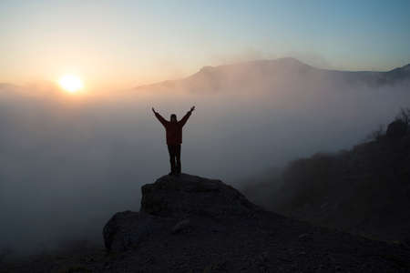 Woman  lifts her arms in victory. She contemplates beautiful sunset in mountains.