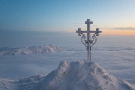 Frosted cross on mountain top. Snowy mountains are folded in mist. This scene inspires.の写真素材