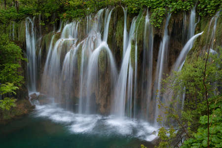 Massive waterfall downs to green lake. Waterfall is surrounded with green foliage.の写真素材