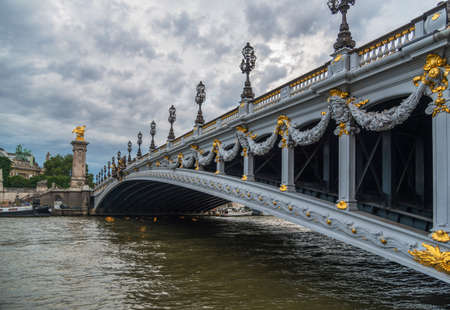 Pont Alexandre III  - deck arch bridge that spans the Seine in Paris. Gold bridge decorations stands out against cloudy sky  background.の写真素材
