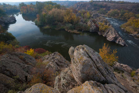 Picturesque river bend in autumn season. Famous Integral  riffle of Southern Bug river. Rocks and highly coloured trees in foreground.の写真素材