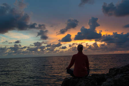 Woman sits as yogi against beautiful sunset over sea background.の写真素材