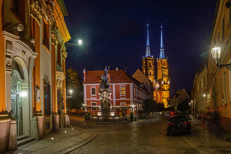 Night scene in Wroclaw. Illuminated old buildings and cathedral. Street cobbled with block stones in foreground.の写真素材