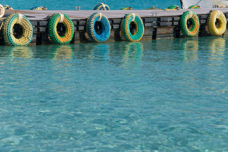 Pier with multicolored tires defending ships during stop. Blue transparent sea in foreground.の写真素材