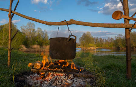 Black pot are heating under fire. Trees, river and sky in background. Scene from travel.の写真素材