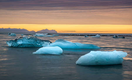 Ice floating in famous Ice Lagoon (Iceland). Orange sunrise in background.
