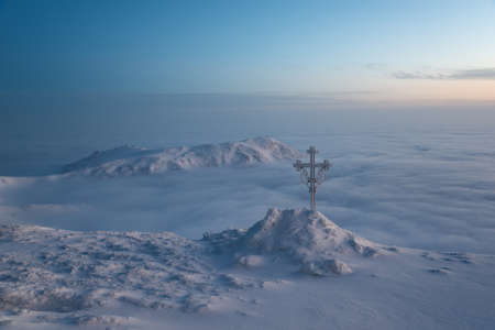 Frosted cross (Christianity symbol) against beautiful sunrise scene in mountains. の写真素材