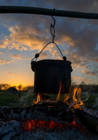 Black pot are heating under fire. Evening in camping. Bright sunset in background.の写真素材