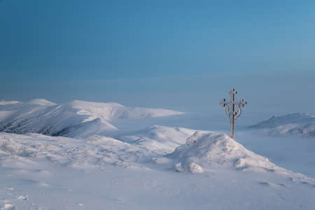 Frosted cross against beautiful sunrise scene in mountains. White mountains and white clouds are illuminated with morning sun.の写真素材