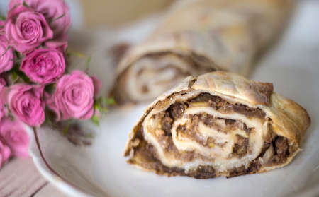 Strudel slice on a white dish. Pink roses lying nearby enliven the culinary composition.の写真素材