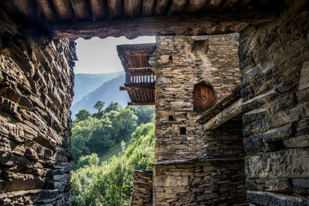 Inside view of Shatili walled city. Dark-lit buildings contrast with lush greenery outside.の写真素材