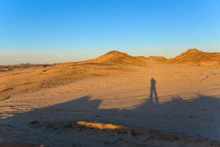 Stone and sand desert with long shadows. Blue sky in background.