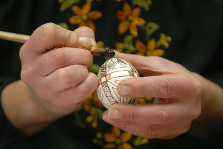 Craftswoman decorates egg before Easter with help of pisachok.