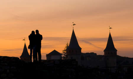 Kamianets-Podilskyi: couple in love at sunset. Only silhouettes of castle towers are visible.