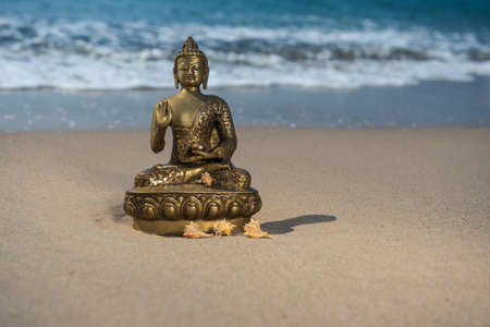 Bronze statuette Buddha on the beach with wavesの写真素材