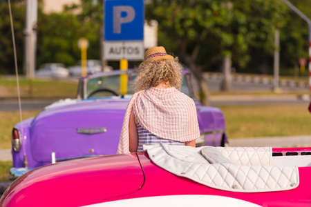 Curly girl on the background of colored cars Cuba, Havana. Back viewの写真素材