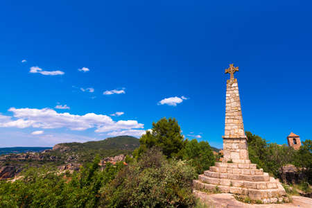 Memorial Cross and Church of Santa Maria de Siurana in Siurana de Prades, Tarragona, Catalunya, Spain. Copy space for text. Isolated on blue backgroundの写真素材