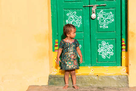 PUTTAPARTHI, ANDHRA PRADESH, INDIA - JULY 9, 2017: Little indian girl on the doorstep of the house. Copy space for textのeditorial素材