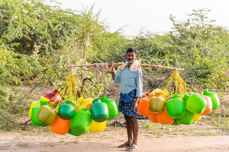 PUTTAPARTHI, ANDHRA PRADESH, INDIA - JULY 9, 2017: Man with buckets for water. Copy space for textのeditorial素材