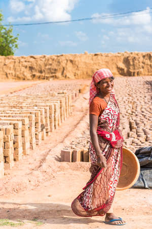 PUTTAPARTHI, ANDHRA PRADESH, INDIA - JULY 9, 2017: Indian woman on a background of drying bricks. Copy space for text. Verticalのeditorial素材