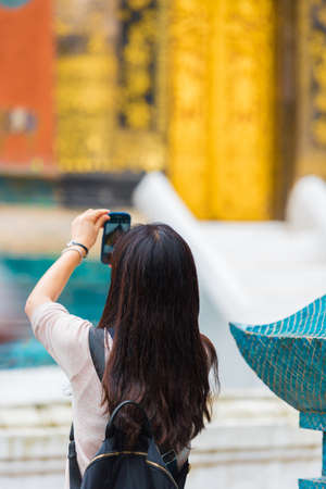 Woman tourist taking pictures of a Buddhist temple in Louangphabang, Laos. Close-up. Verticalの写真素材
