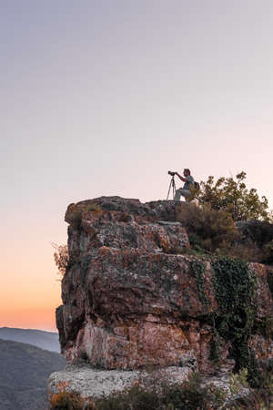 SIURANA DE PRADES, SPAIN - OCTOBER 5, 2017: A photographer on a rock takes pictures of the landscape at sunset. Copy space for text. Verticalのeditorial素材