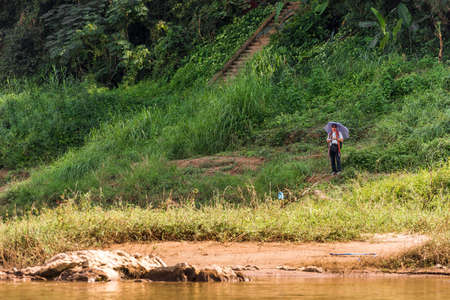 LOUANGPHABANG, LAOS - JANUARY 11, 2017: A man with an umbrella on the bank of the of the Nam Khan river. Copy space for textのeditorial素材