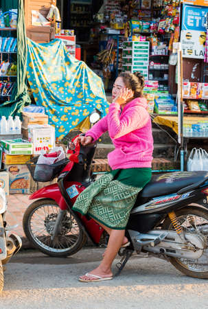LUANG PRABANG, LAOS - JANUARY 11, 2017: Women with a motorcycle on a city street. Verticalのeditorial素材