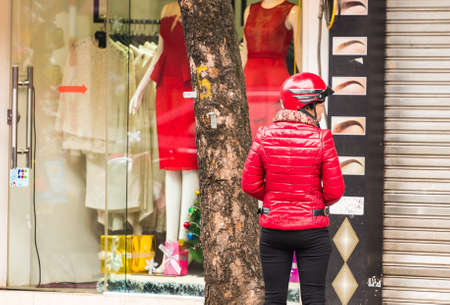 HANOI, VIETNAM - DECEMBER 16, 2016: A woman in a red jacket in the background of shops. Copy space for text. Back viewのeditorial素材