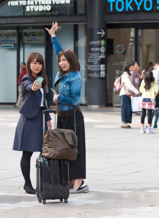 TOKYO, JAPAN - NOVEMBER 7, 2017: Two girls with suitcases take pictures of themselves.のeditorial素材