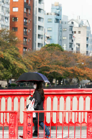 TOKYO, JAPAN - OCTOBER 31, 2017: Girl under an umbrella walking on a bridgeのeditorial素材
