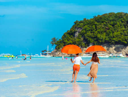Two girls under umbrellas on a sandy beach, Boracay, Philippines. Copy space for text. Back viewの写真素材