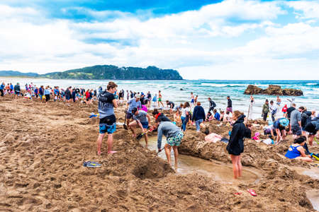 COROMANDEL, NEW ZEALAND - OCTOBER 13, 2018: Tourists dig holes in the volcanic sand on the Hot Water...