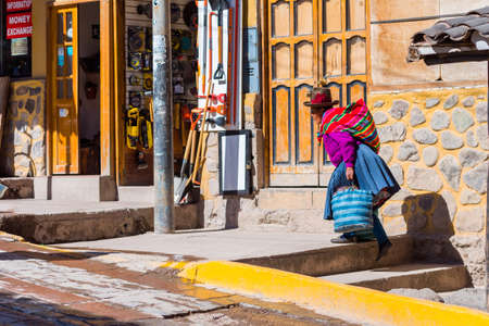 OLLANTAYTAMBO, PERU - JUNE 26, 2019: Peruvian woman cholita dressed in traditional colorful cloth, carries bagsのeditorial素材