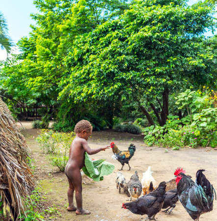 TANNA ISLAND, VANUATU - JULY 21, 2019: Naked little girl feeding chickens in the village of Yakelのeditorial素材