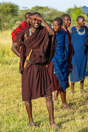 NGORONGORO, TANZANIA - February 15, 2020: A smiling Masai Man looking to the Camera and hold him Hand at the Head, a Group of Masai People prepare a Traditional Warrior Danceのeditorial素材