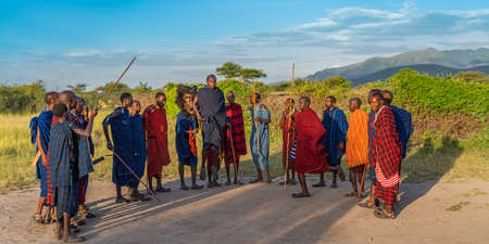 NGORONGORO, TANZANIA - February 15, 2020: A Massai Man in blue black Cape jump very High, a Group of Massai People, one with Ostrich Feather Headgear watching him, Background a Beautiful Sunset Landscape, selected focusのeditorial素材